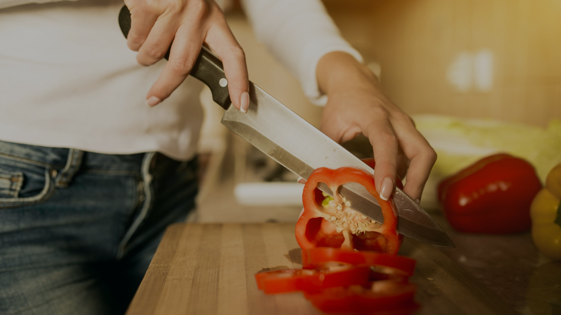 Person cutting a red bell pepper with a knife on a wooden cutting board.