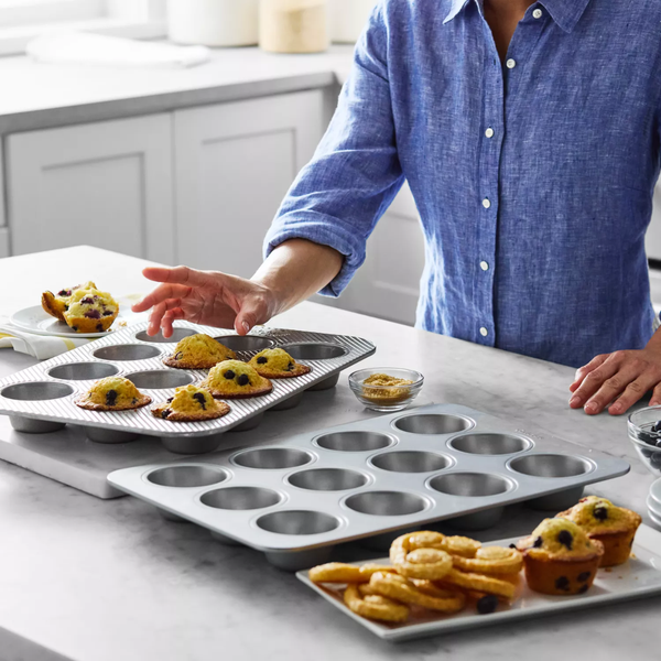 Person arranging muffin tins with baked goods on a kitchen counter