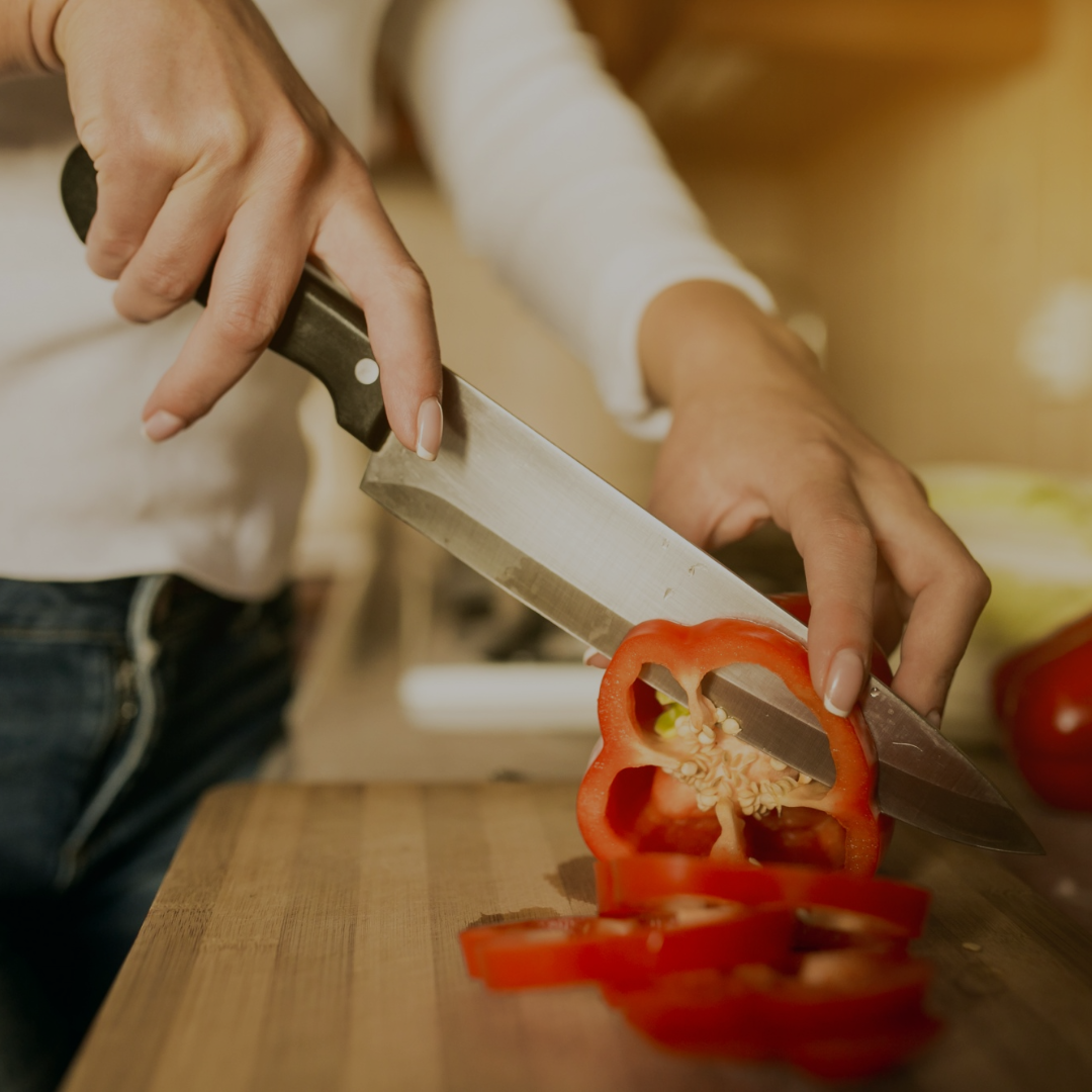 Person slicing a red bell pepper with a knife on a wooden cutting board.