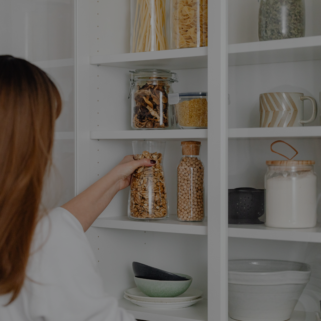 Person reaching for a jar of food on a well-stocked kitchen shelf.