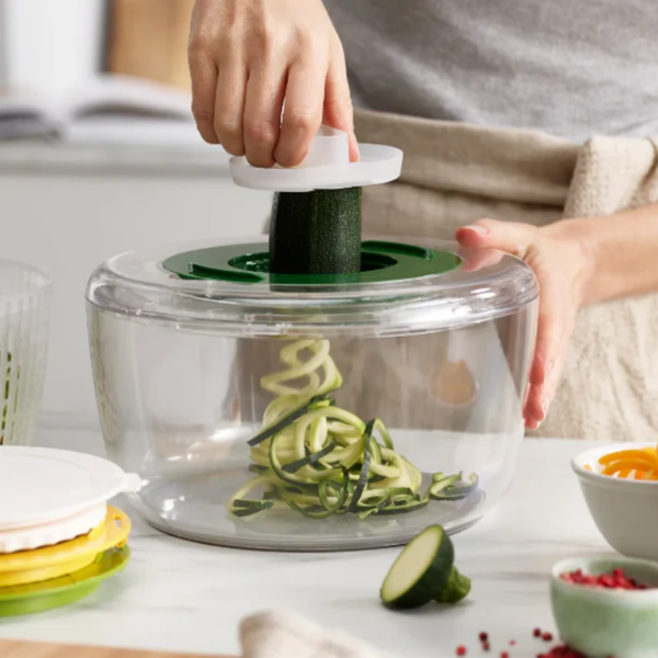Person using a spiralizer to make zucchini noodles on a kitchen counter.