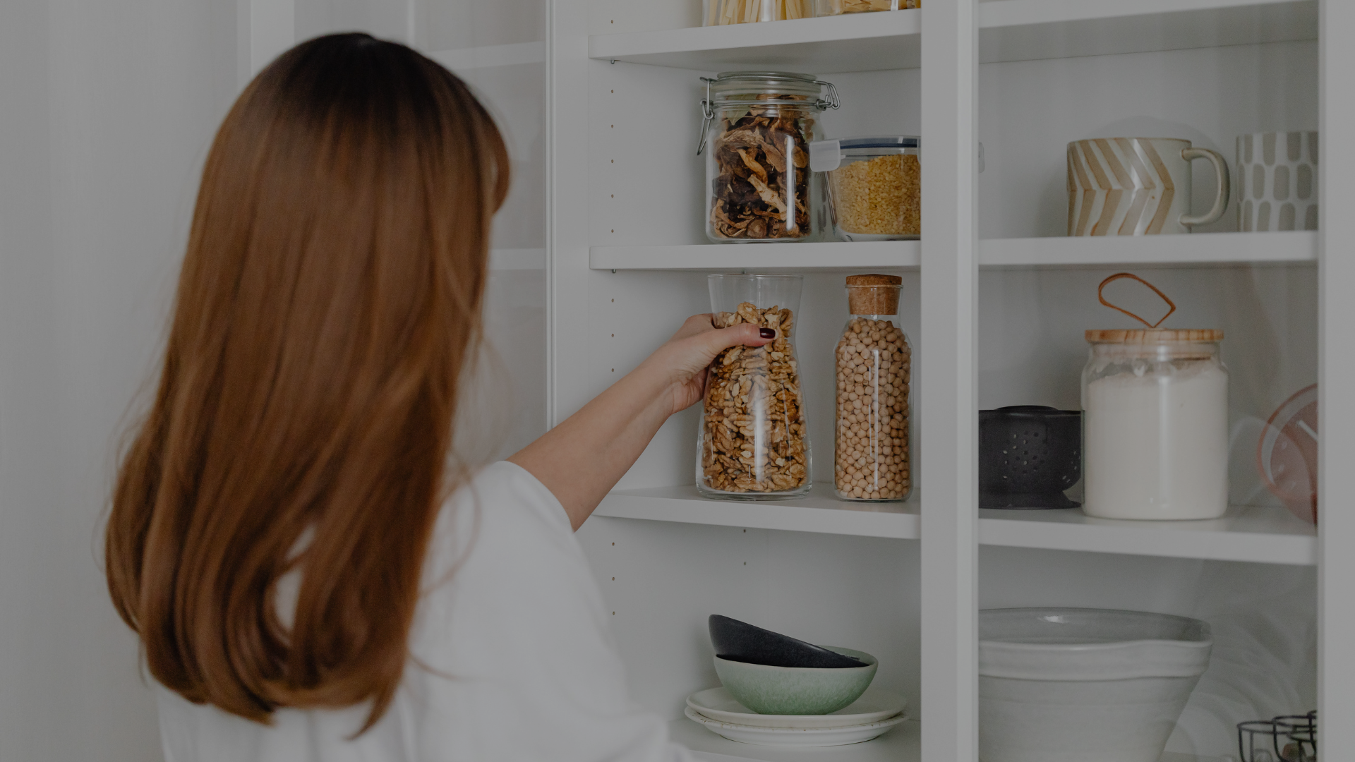 Person reaching for a jar on a kitchen shelf filled with various items.